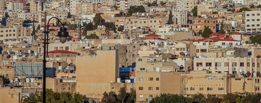 View of the dense urban landscape of Jerash featuring residential buildings, rooftops with water tanks, and a street lamp in the foreground in Jerash, Jerash Governorate, Jordan.