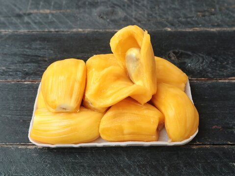 Fresh sweet ripe jackfruit slices arranged on a white plate over a rustic dark wooden table background. Delicious tropical fruit snack, healthy organic food photography