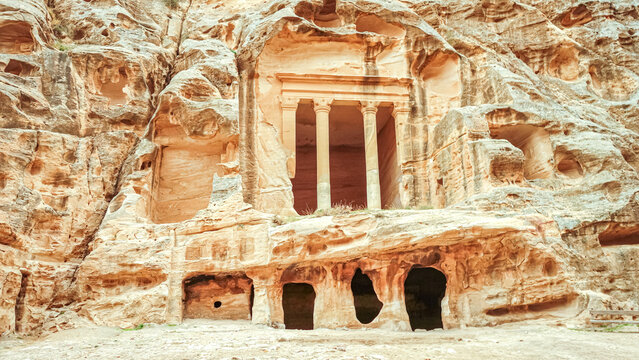 View of an ancient Nabataean rock-cut tomb facade featuring carved columns and weathered sandstone cliffs in Wadi Musa, Ma'an Governorate, Jordan.