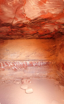 View of the interior of a historic rock-cut chamber featuring intricate red and orange sandstone layers and natural rock formations in Wadi Musa, Ma'an Governorate, Jordan.