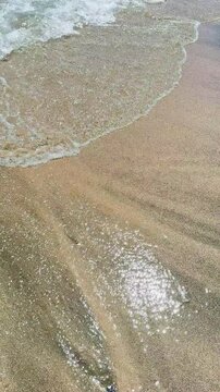 Waves gently lap at the sandy shore under the bright sun. The surface of the water sparkles in the sunlight, creating a shiny view. The scene captures a warm day by the beach.
