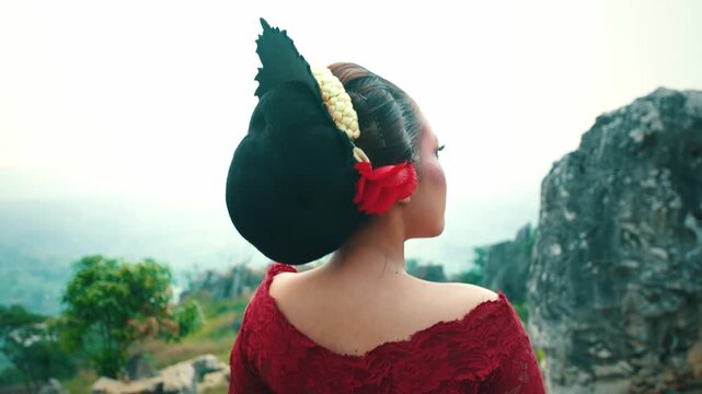 Profile view of an elegant Indonesian dancer showing off her traditional makeup and hair accessories against a bright sky and rocky background.