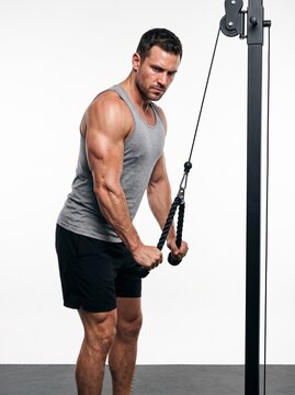 Muscular man performing cable tricep pushdown with focused concentrated expression isolated on plain white background bright studio arm workout gym strength training fitness