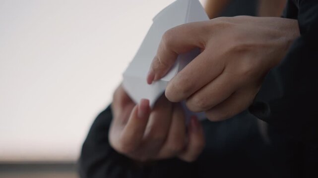 Woman carefully manipulates white paper object revealing its geometric folds and structure. Her hands move deliberately to display details of crafting or examining origami piece against soft