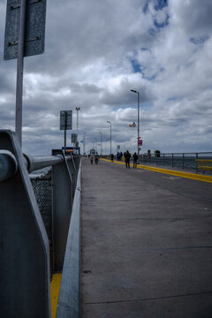 View of Muelle de Puerto Madryn with people walking along the concrete pier under a cloudy sky in Puerto Madryn, Chubut Province, Argentina.