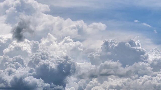 Billowing white cumulus cloud formations swell and boil dynamically across sky, time-lapse. Ragged dark cloud layers drift rapidly across foreground, creating deep layers and textured dimensions