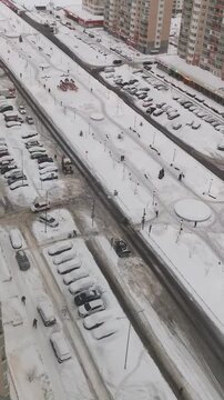 Snowplow clears a road through a snow-covered residential neighborhood. Winter street maintenance among parked cars and apartment buildings.