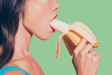 Close-up profile side view cropped portrait of nice alluring adorable glamorous charming attractive sweet lovely wavy-haired lady holding biting banana red lips isolated over pink pastel background © deagreez