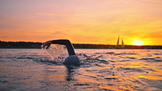 A young athlete swims with unwavering determination during an evening training session. The serene sunset and rhythmic strokes against a majestic bridge backdrop capture the essence of perseverance.