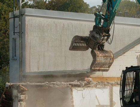 View of an excavator with a hydraulic grapple attachment demolishing a concrete wall at a construction site in Garching, Bavaria, Germany.