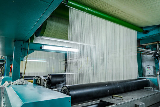 View of a denim factory production line with white threads running through industrial rollers and machinery in a textile mill in Karachi, Sindh, Pakistan.