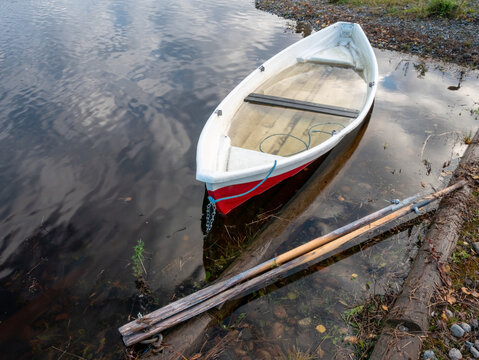 View of a row boat partially submerged in river water after a flood, with wooden oars resting on the muddy bank in Muhos, North Ostrobothnia, Finland.