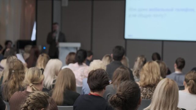 Listeners face a speaker beside projected slides in mostly stationary framing.