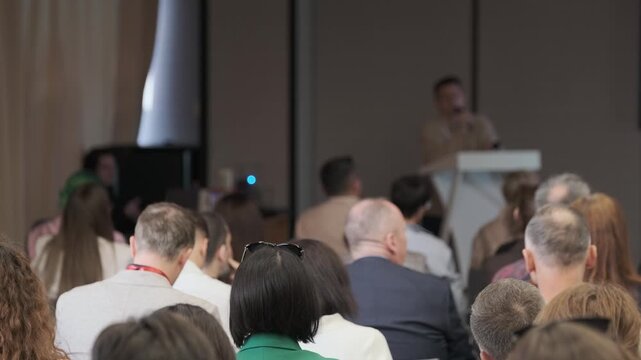 Seated conference attendees face the lectern as people move nearby during rightward camera panning.