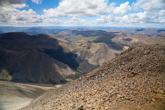 View of the rugged landscape near San Luis Peak and West Willow Creek Trailhead with rocky slopes, distant mountain ranges, and a cloudy blue sky in Creede, Colorado, United States.