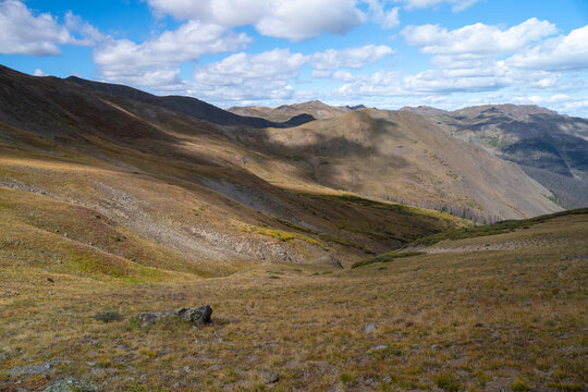 View of San Luis Peak and the rugged mountain landscape near West Willow Creek Trailhead with golden grassy slopes and shadows under a blue sky in Creede, Colorado, United States.