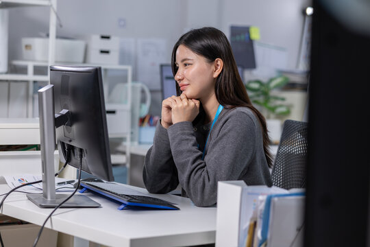 Asian woman working at computer in modern office, focused and thoughtful during quiet workday