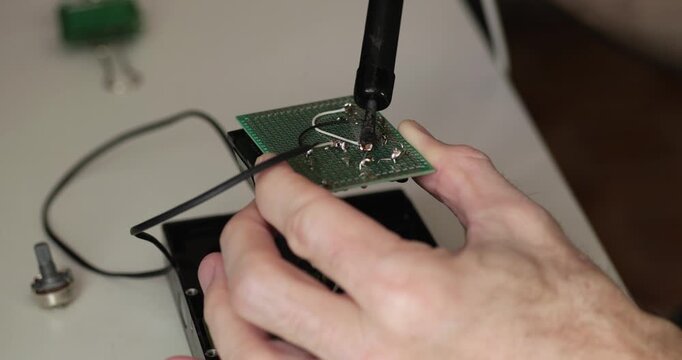 Closeup soldering circuit board during electronics repair. Skilled hands connect wires on printed circuit board in workshop. DIY technology footage shows precision, maintenance, and engineering craft.