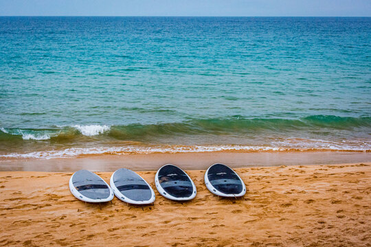 View of four stand-up paddleboards resting on the sandy beach with gentle waves rolling onto the shore in Maui County, Hawaii, United States.