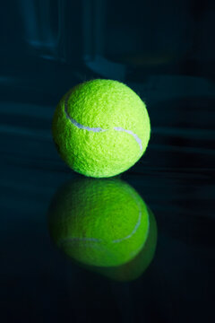 Neon tennis ball on a dark glossy surface.