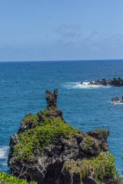 View of a volcanic sea stack covered in lush green vegetation rising from the deep blue Pacific Ocean in Maui County, Hawaii, United States.