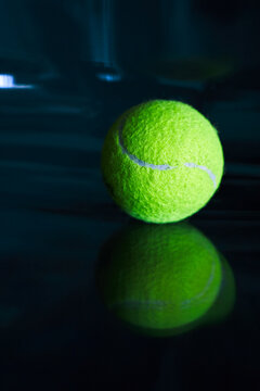 Neon tennis ball on a dark glossy surface.