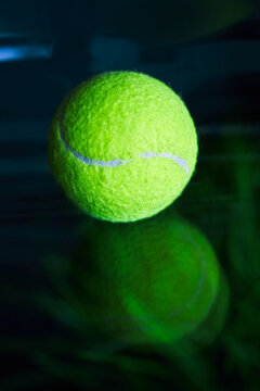 Neon tennis ball on a dark glossy surface.