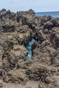 View of rugged volcanic rock formations along the coastline with the blue ocean visible through a gap in Maui County, Hawaii, United States.