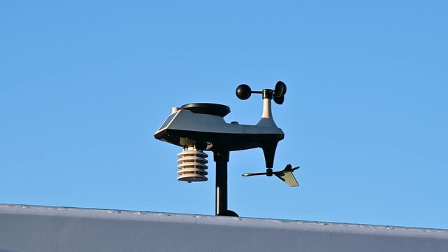Automatic weather station with rotating cup anemometer and wind vane installed outdoors under blue sky. 4K slow motion footage useful for climate projects and meteorology broadcasts