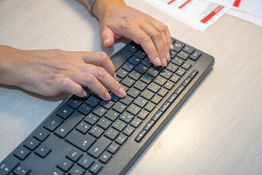 Two hands type on a black computer keyboard on a light-colored desk. Close-up illustrating computer use, office work, and data entry.