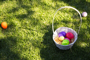 White woven basket is sitting right on sunlit grassy lawn holding colorful plastic eggs in straw © WavebreakMediaMicro