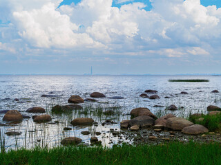 The Gulf of Finland viewed from a rocky shore  the silhouette of the Lakhta Center in St. Petersburg is visible on the horizon. Shallow water featuring boulders, pebbles, and coastal vegetation © Shauerman