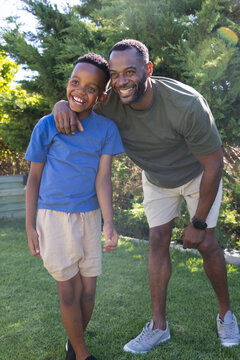 African American father and son standing and smiling on manicured backyard lawn showing wristwatch