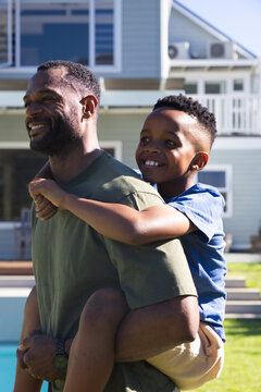 African American father and child playing, father wearing olive T-shirt carrying boy by pool edge