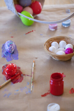 Woven basket is holding seven eggs on kraft paper with painted eggs and paintbrush nearby