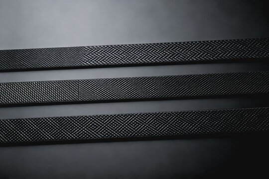 Three black textured strips with distinct patterns arranged in parallel on a plain gray background, showcasing different surface textures.