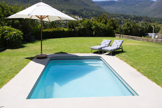 Rectangular in-ground swimming pool is sparkling on tiled deck under large white umbrella shadow