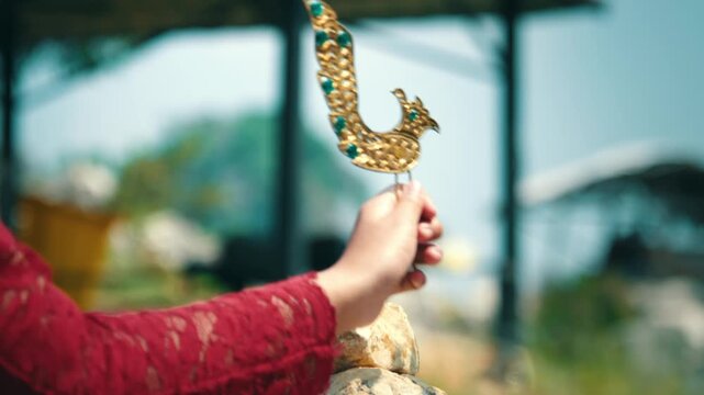 A woman's hand holding and adjusting a golden bird hair ornament, showcasing the intricate details of the traditional Indonesian bridal jewelry.