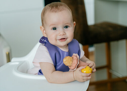 Baby holding fruit nibbler in high chair