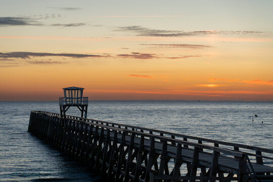 Luc-Sur-Mer, France - 08 08 2026:  View of a wooden pier in front of the sea, a colorful sunrise and Le Havre city far away