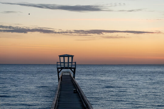 Luc-Sur-Mer, France - 08 08 2026:  View of a wooden pier in front of the sea, a colorful sunrise and Le Havre city far away