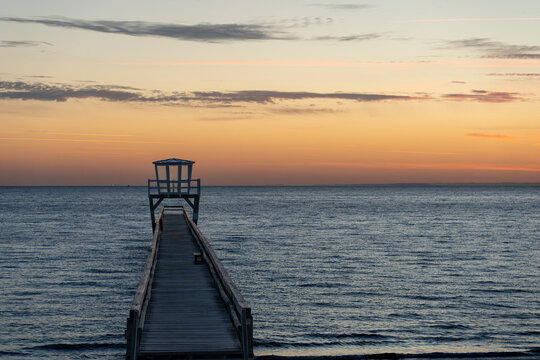 Luc-Sur-Mer, France - 08 08 2026:  View of a wooden pier in front of the sea, a colorful sunrise and Le Havre city far away