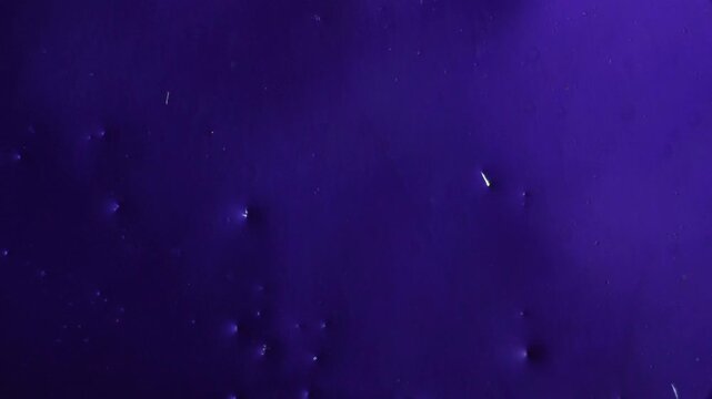 Real time polarized light microscopy of fluid solution fast flow displaying microfluidic stream dynamics and erosion of tiny mineral crystal structures over purple background science concept
