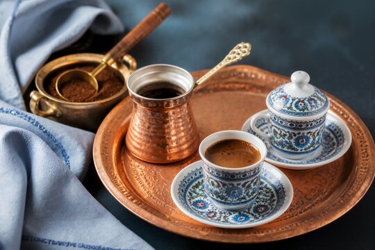 Turkish coffee served in traditional patterned cup on copper tray with cezve. Freshly brewed dark espresso on dark table