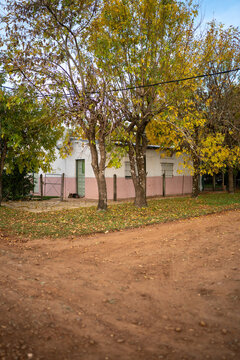 View of a small house with a pink and white facade surrounded by autumn trees and a dirt road in Guaviravi, Corrientes Province, Argentina.