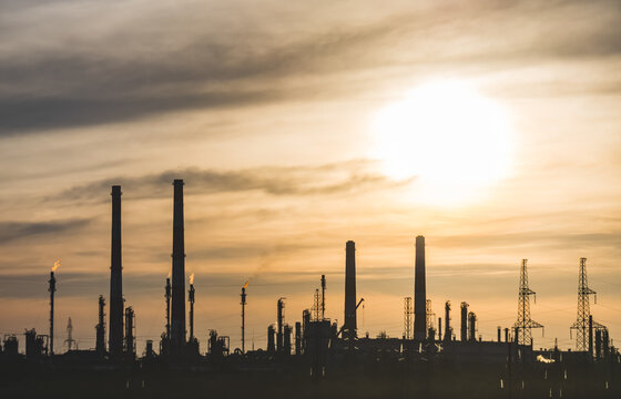Oil refinery with tall flare stacks and chimneys in the Kazakh steppe; industrial facility at sunset with flames burning from the stacks
