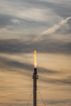 Oil refinery with tall flare stacks and chimneys in the Kazakh steppe; industrial facility at sunset with flames burning from the stacks