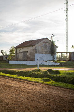 View of a historic, weathered building with a rusty roof and white-painted base situated near a dirt road in Guaviravi, Corrientes Province, Argentina.