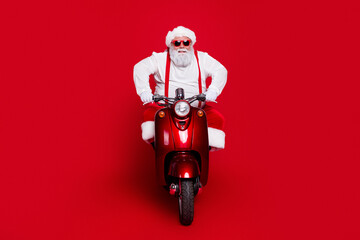 Obraz premium Santa Claus riding a red scooter wearing sunglasses and festive outfit against a bold red background, playful Christmas portrait conveying fun, holiday spirit and modern seasonal style