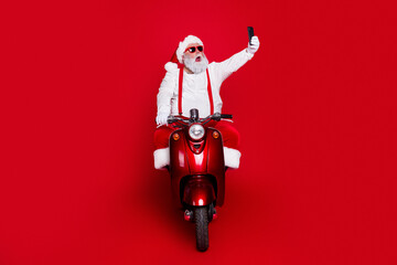 Obraz premium Santa Claus on a red scooter taking a selfie while wearing sunglasses and a festive costume against a red background